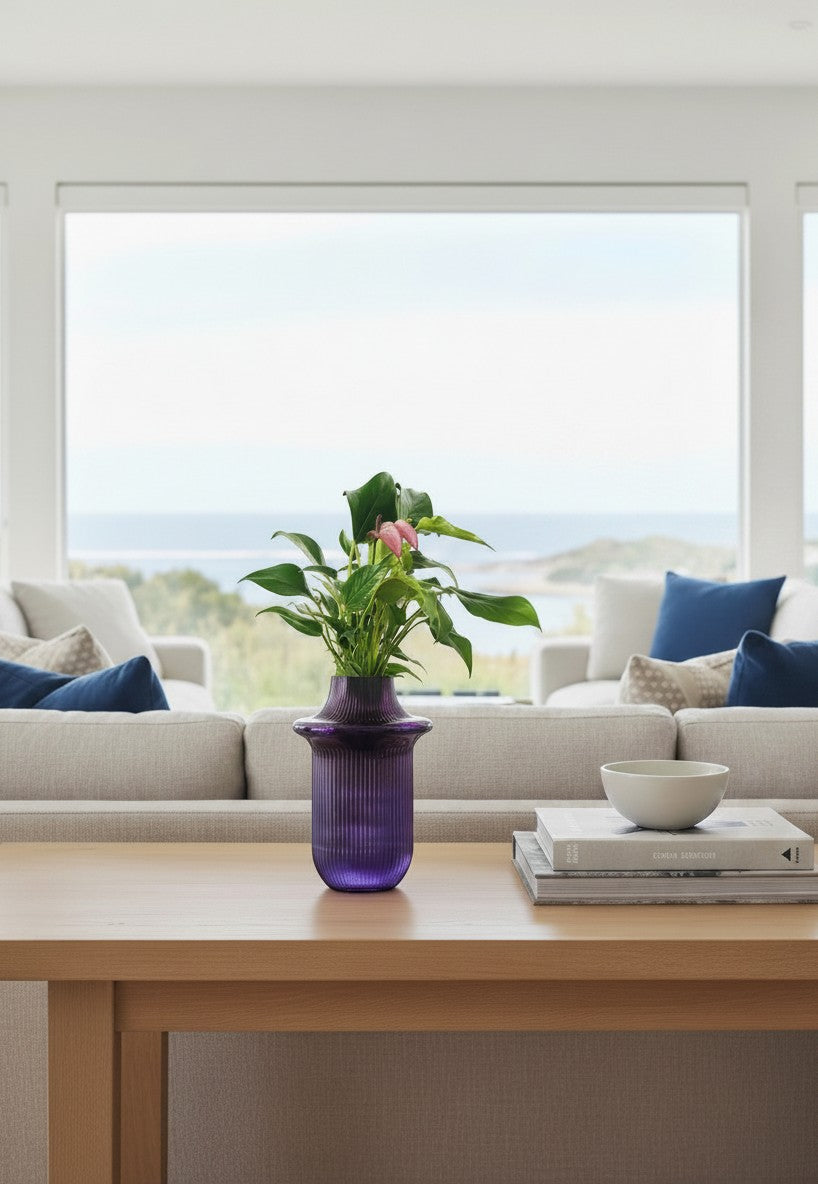 Wanderlust Co. Soho Grape Vessel, a ribbed purple glass vase holding a plant on a wooden table in a bright living room.